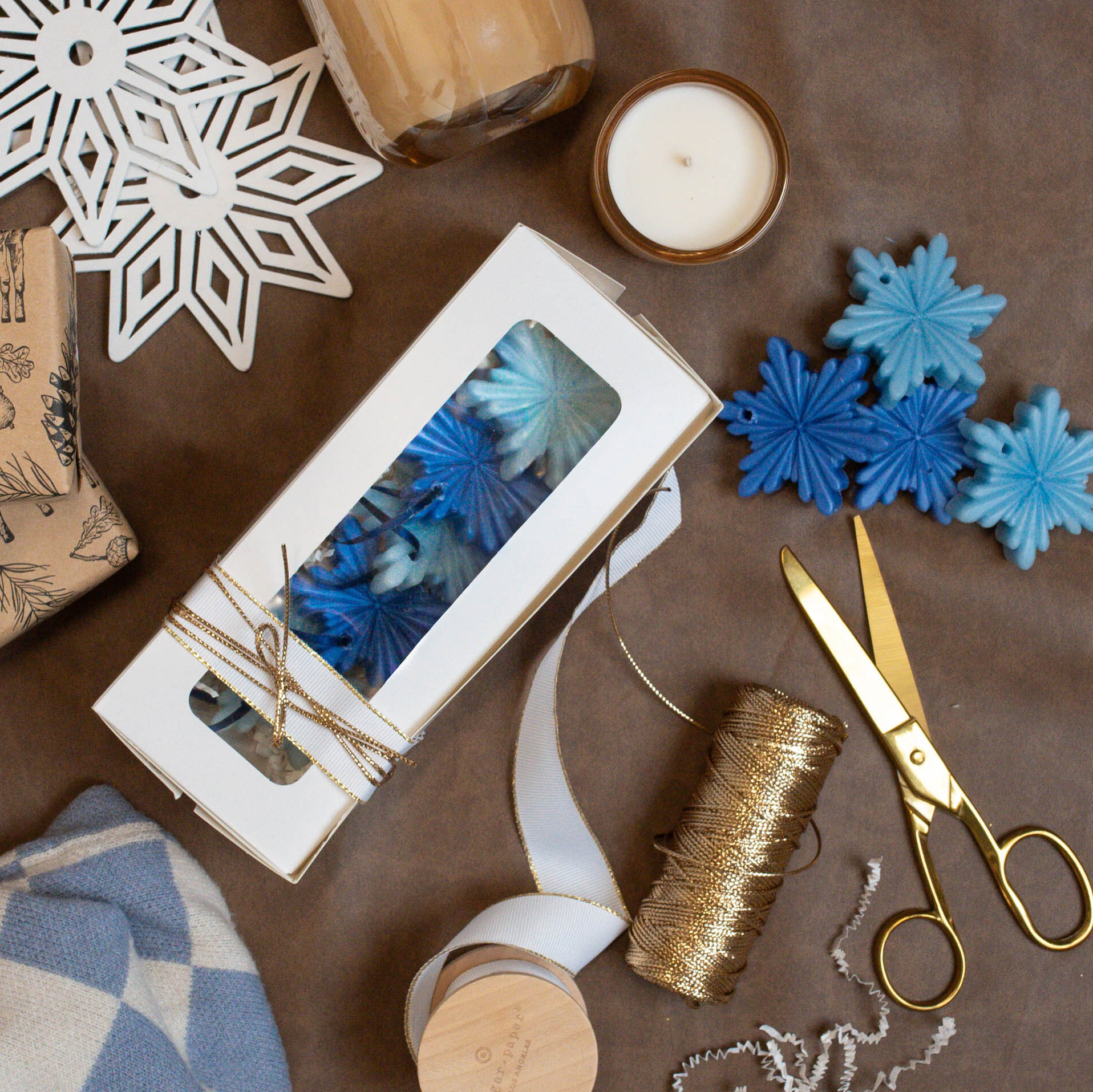Top down view of snowflake beeswax ornaments being wrapped in a gift box.